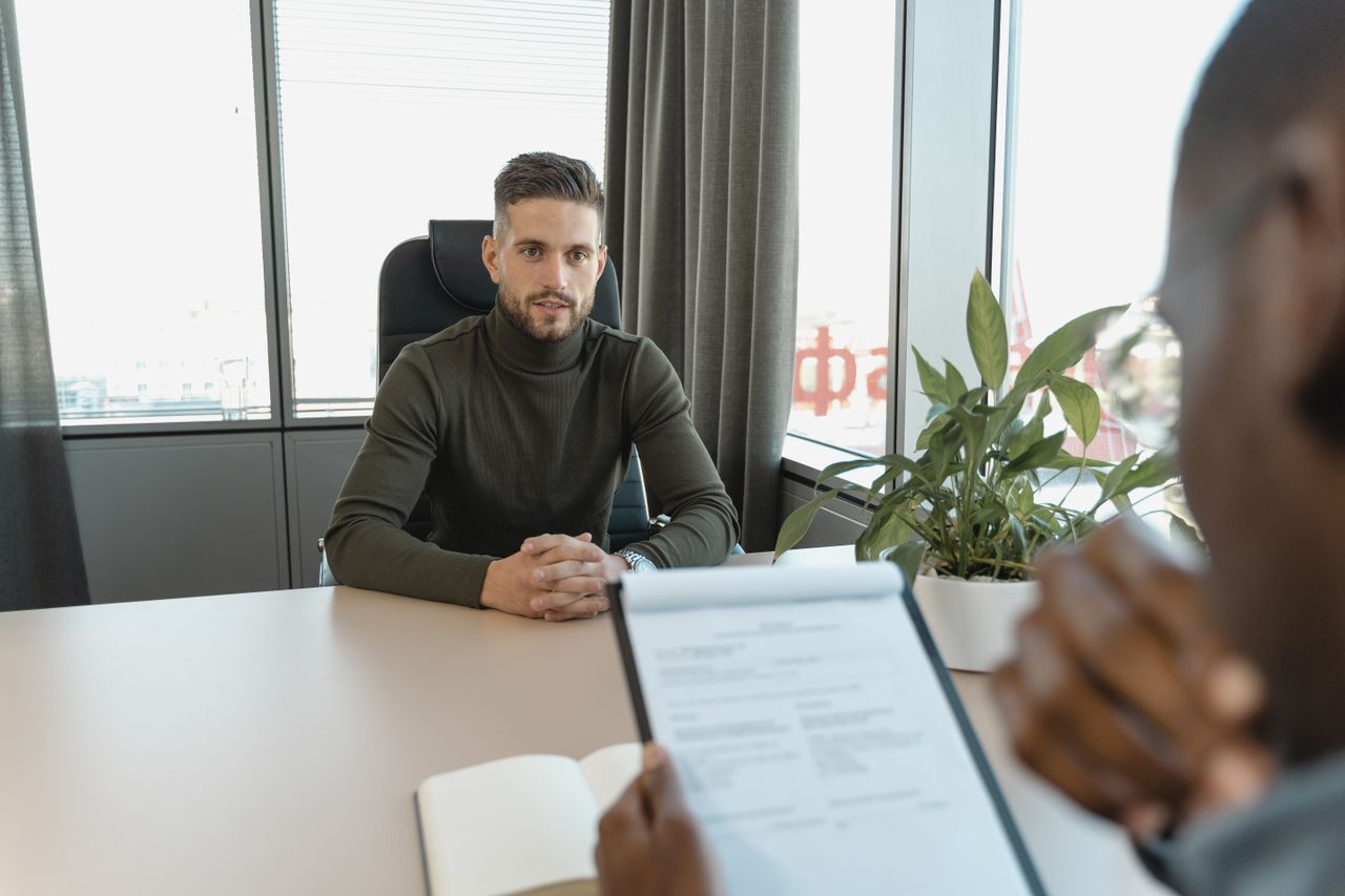 why-choose-us Professional man in turtleneck at office desk during an interview.